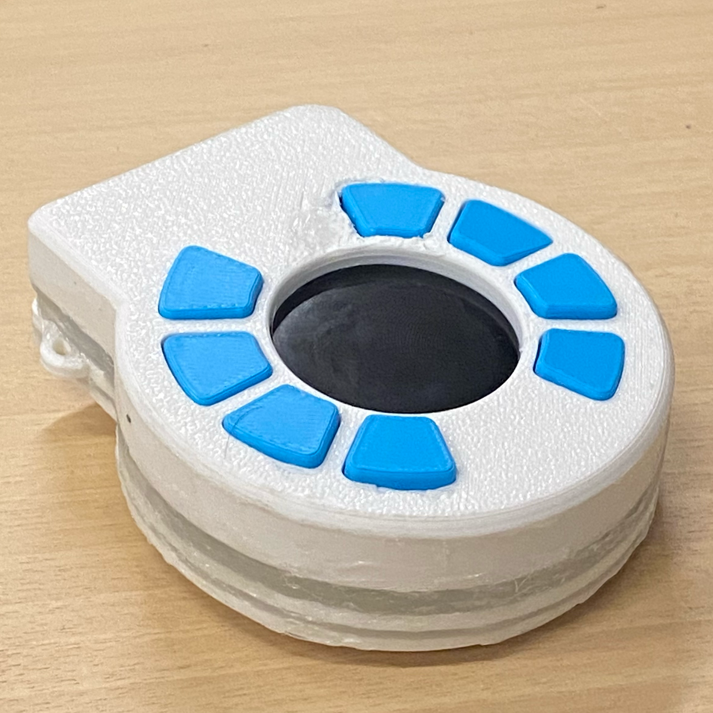 A tiny white circular device with blue buttons, resembling a maimai arcade machine.
