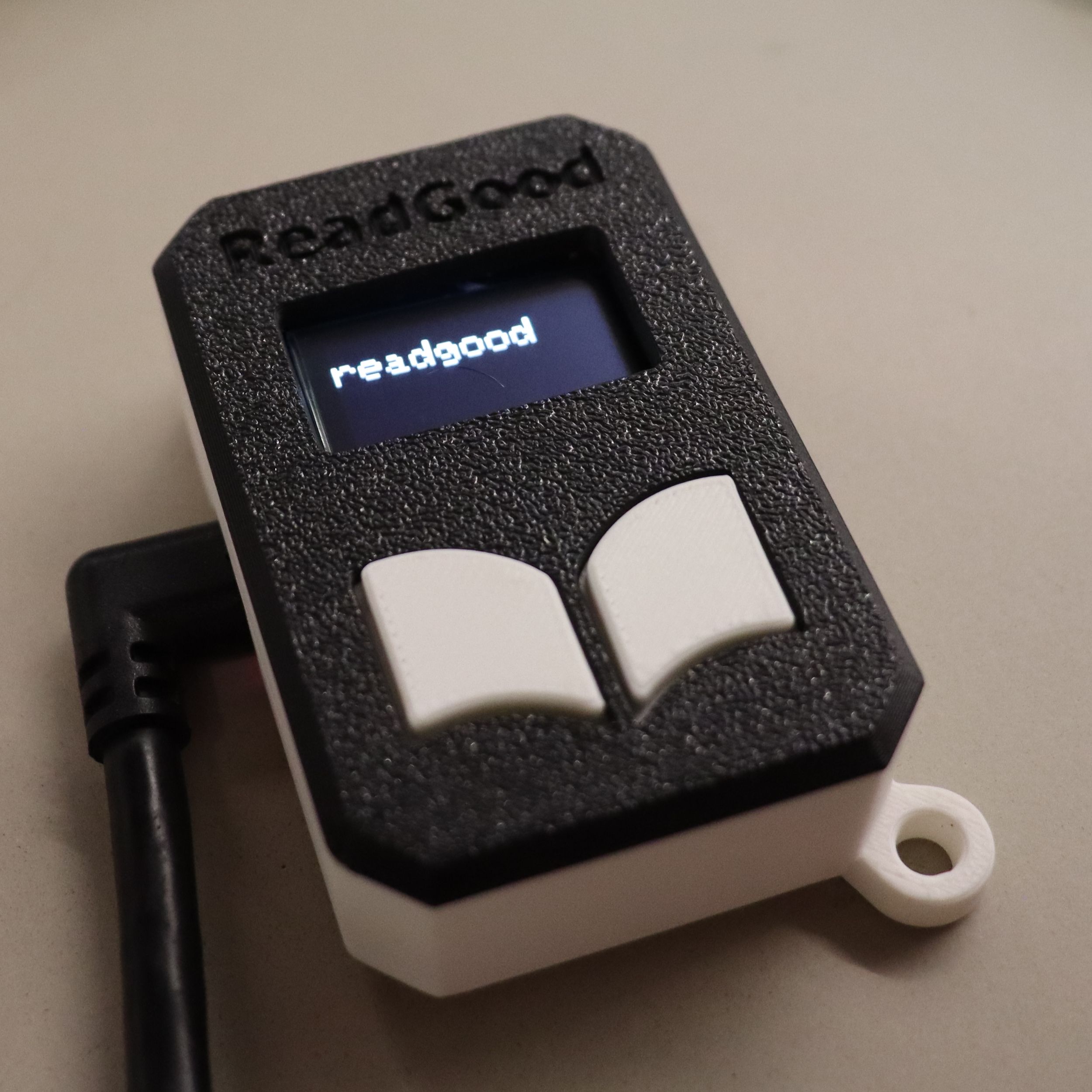 A black-and-white mini e-reader with a small screen and two white buttons resembling an open book.